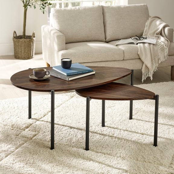 Two wooden nesting tables with a cup and books on a light-colored rug in a living room.