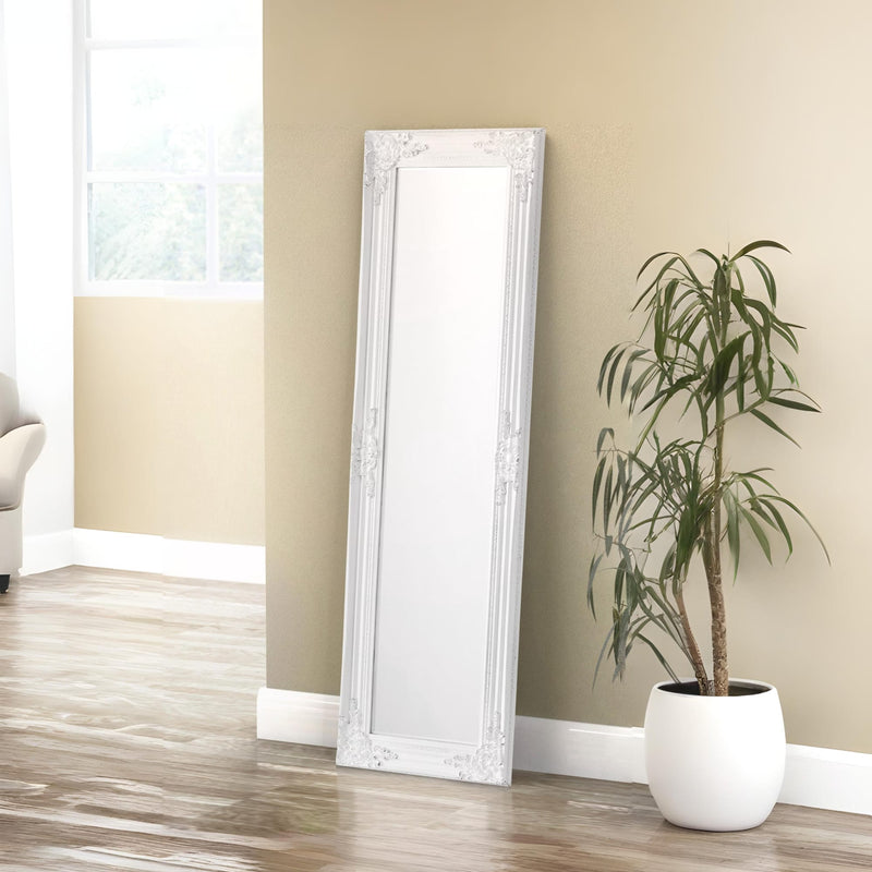White floor mirror leaning against a beige wall next to a potted plant on a wooden floor.