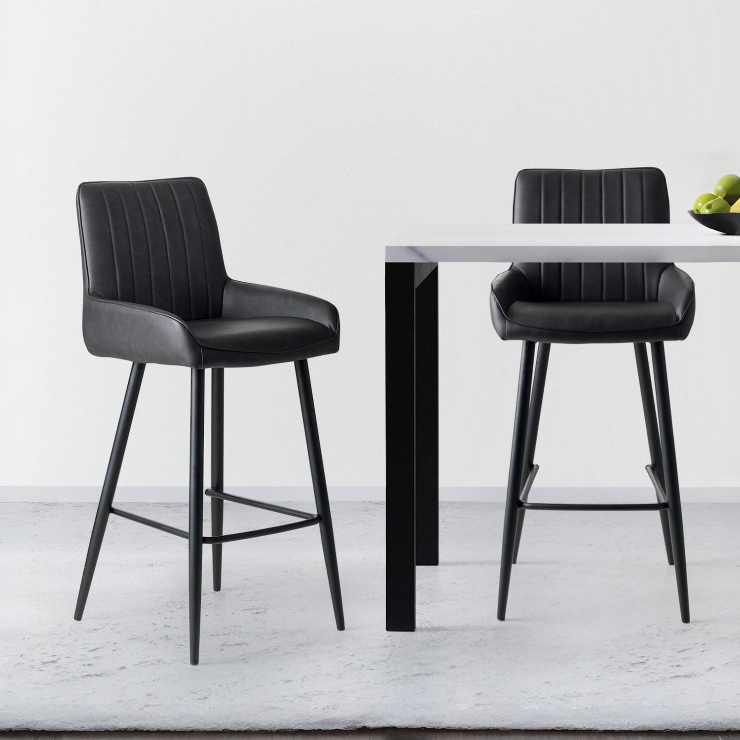 Two black bar stools in front of a small round table on a light gray floor.