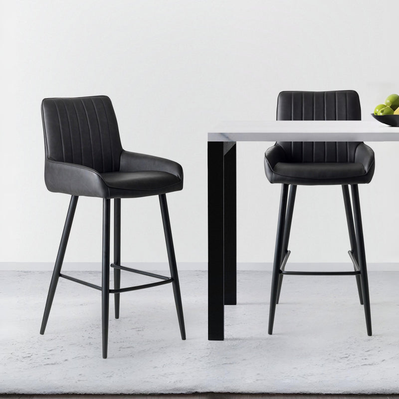 Two black bar stools in front of a small round table on a light gray floor.
