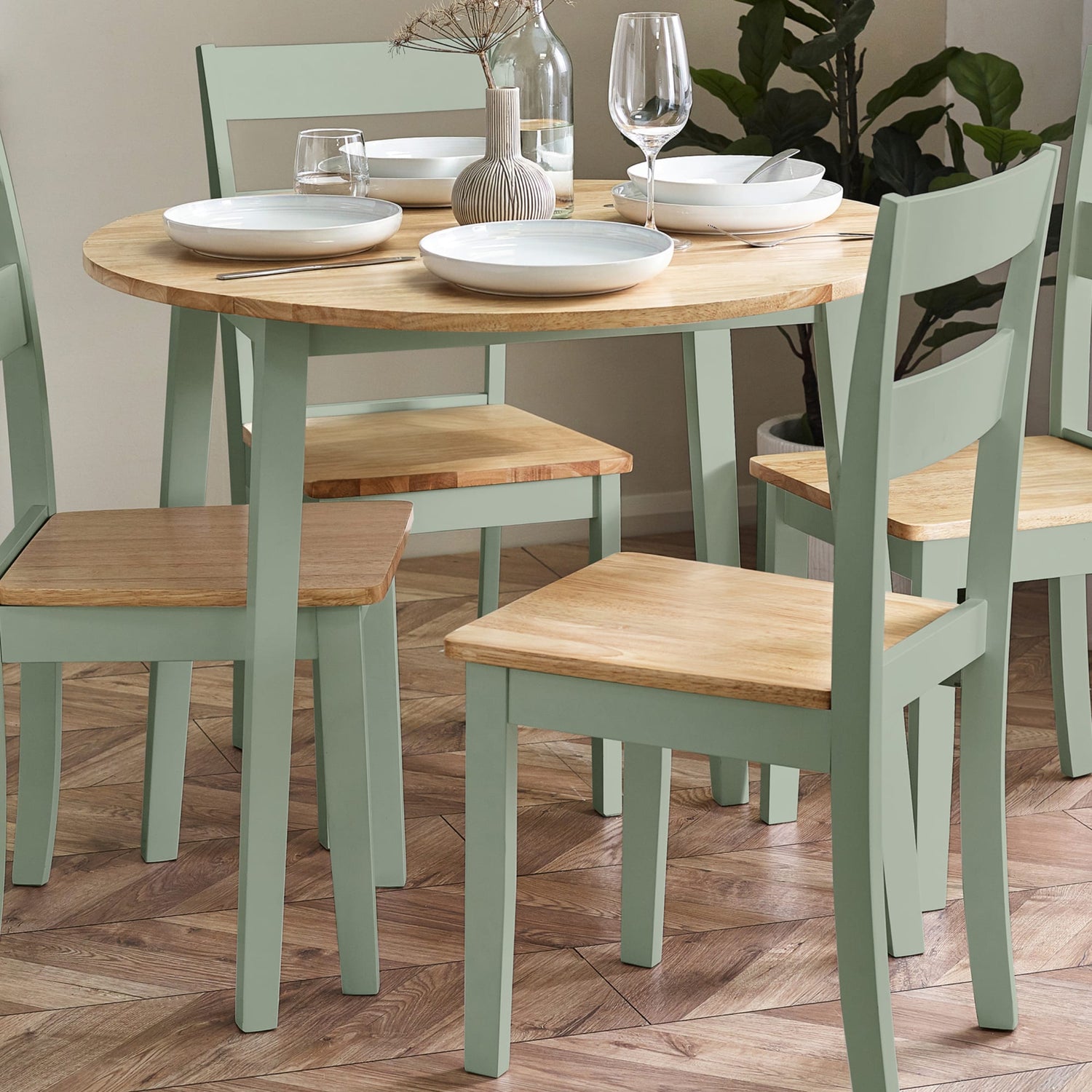 Round wooden dining table with four matching chairs on a wooden floor.