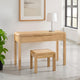 Wooden desk with two drawers and a matching stool in a room with a plant and framed picture.