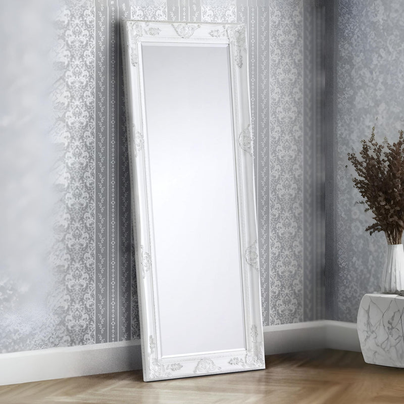 Decorative white mirror leaning against a wall with floral wallpaper.