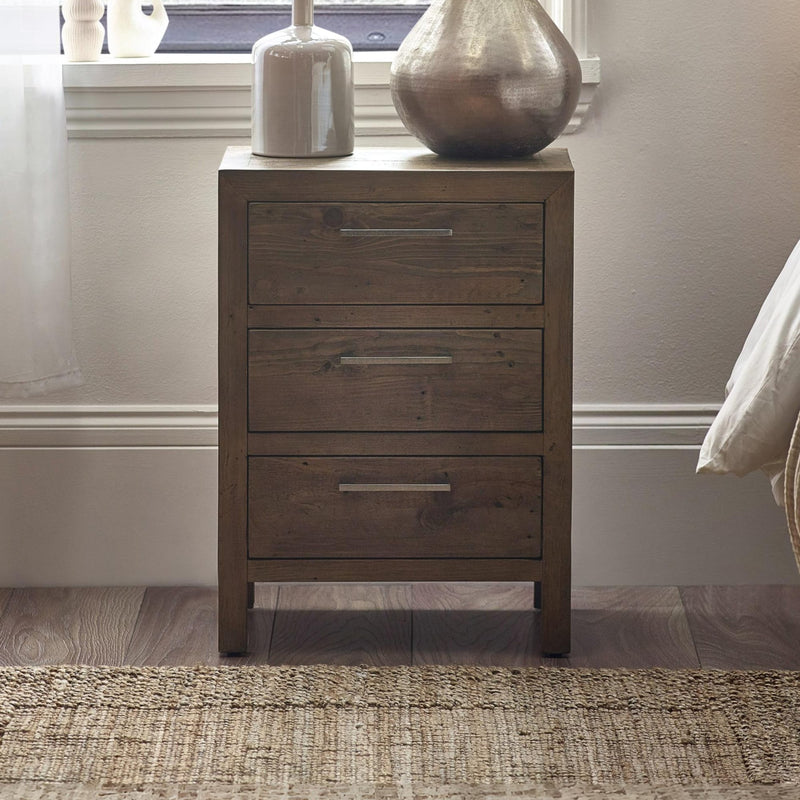 Wooden nightstand with three drawers against a neutral wall.