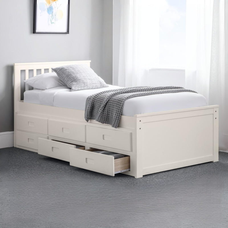 White bed with storage drawers in a room with a gray carpet and a framed picture on the wall.