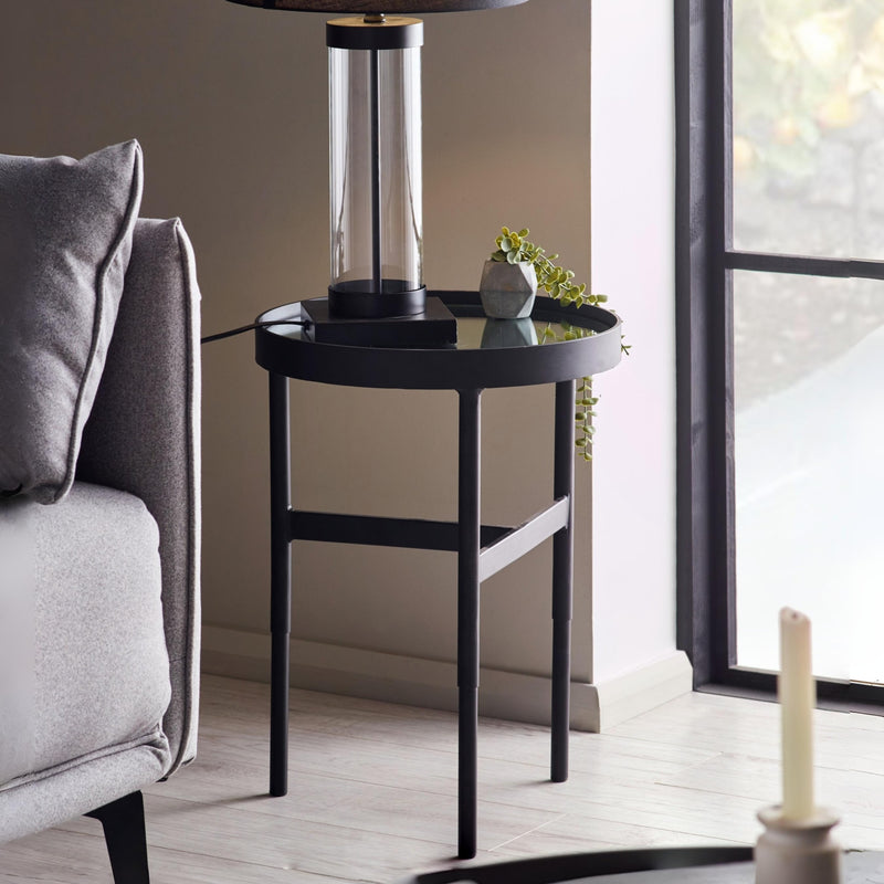 Black side table with a lamp and plant next to a gray sofa in a living room.
