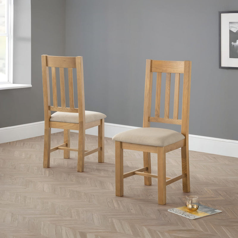 Two wooden chairs with beige cushions on a wooden floor against a gray wall.