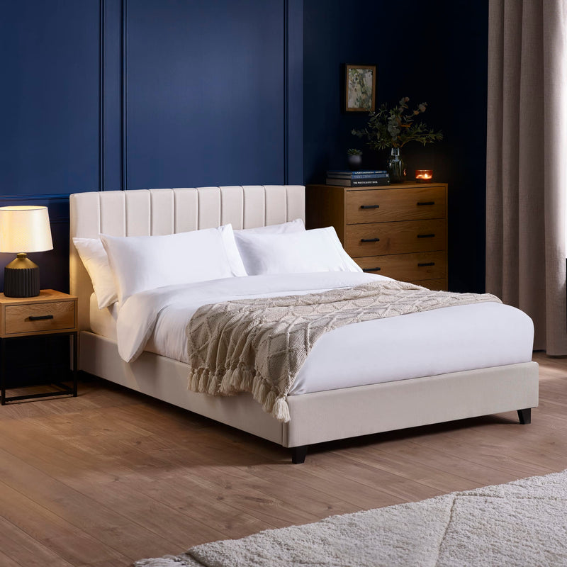 Neatly made bed with white bedding and beige blanket in a bedroom setting.
