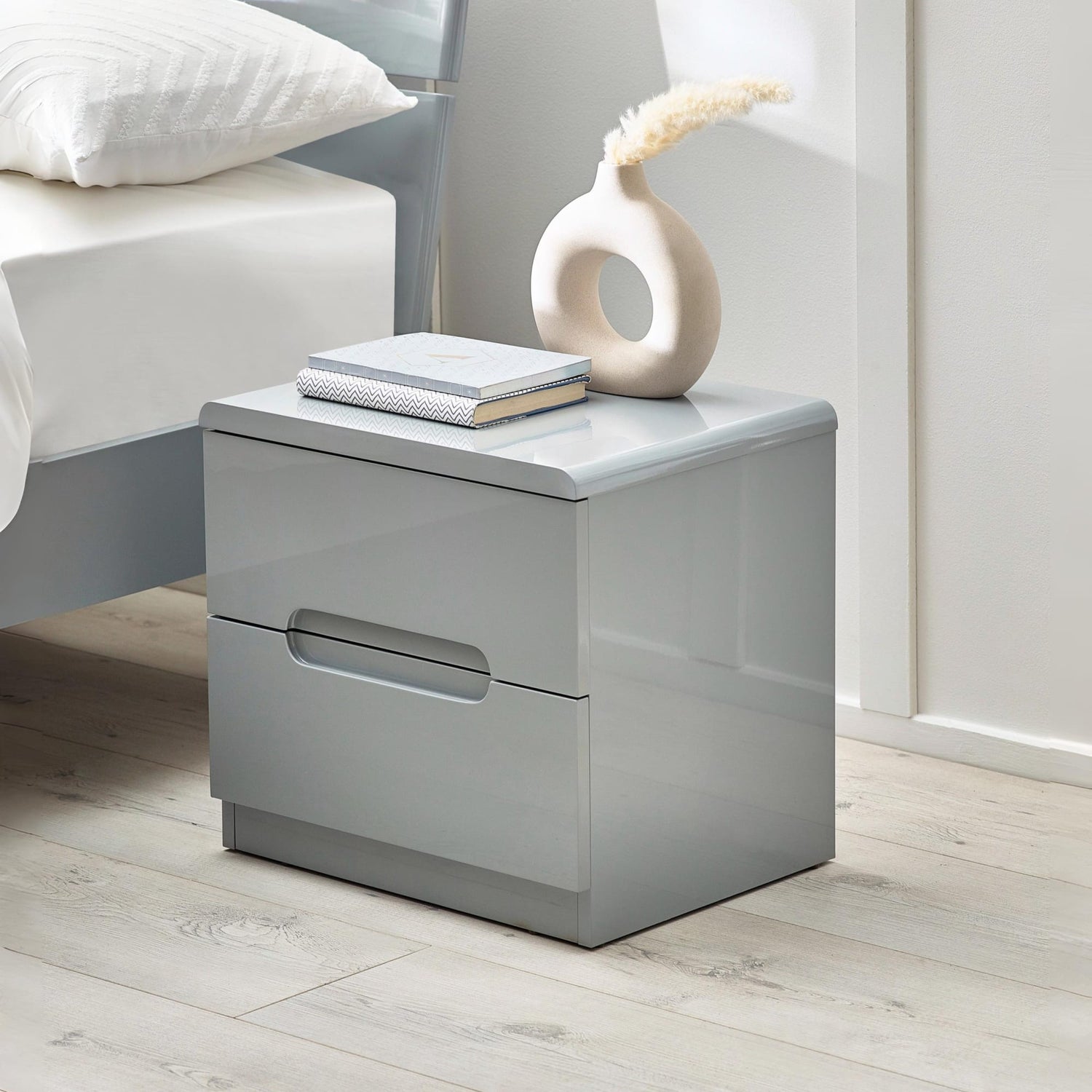 Gray nightstand with a drawer, books, and decorative vase in a bedroom setting.