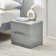 Gray nightstand with a drawer, books, and decorative vase in a bedroom setting.
