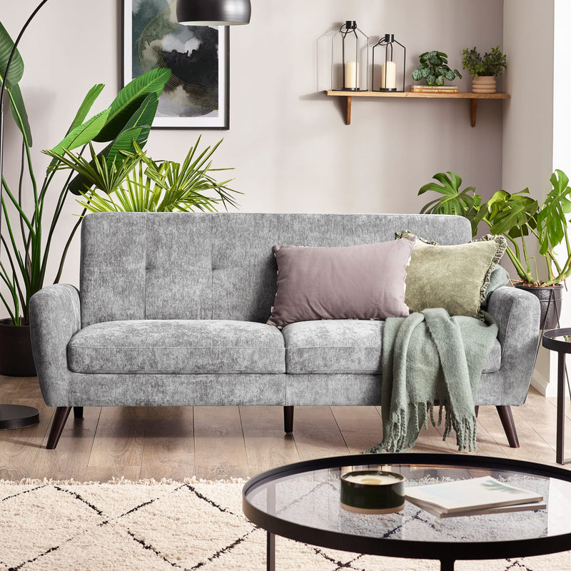 Gray sofa with decorative pillows and a blanket in a living room setting with plants and a coffee table.