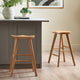 Two wooden bar stools in front of a gray kitchen island with a plant and books on top.