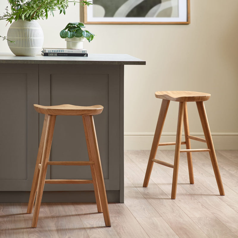 Two wooden bar stools in front of a gray kitchen island with a plant and books on top.