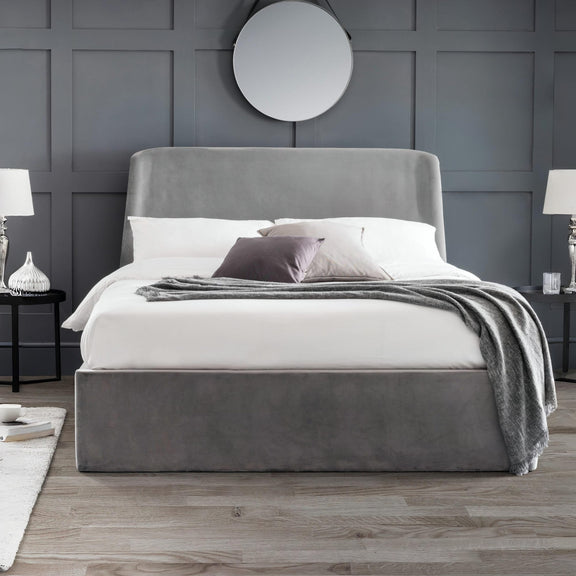 Gray upholstered bed with white bedding in a room with gray walls and wooden flooring.