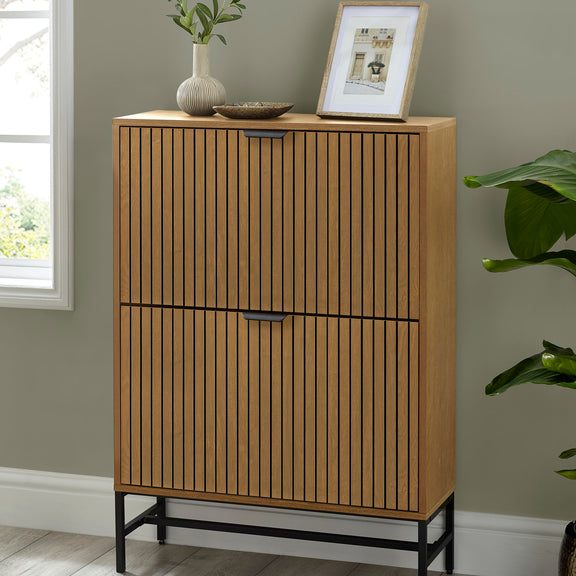 Wooden cabinet with two doors against a gray wall with a plant and framed picture on top.