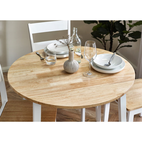 Round wooden dining table set with chairs, plates, glasses, and a vase in a room.