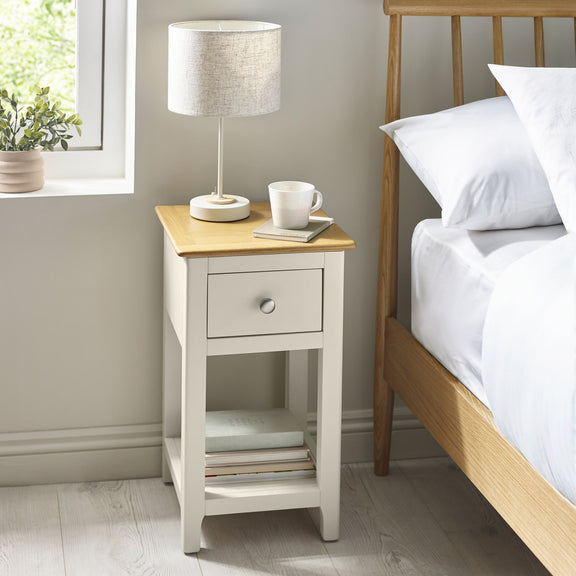 White wooden bedside table with oak top, single drawer and lower shelf beside bed
