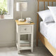 White wooden bedside table with oak top, single drawer and lower shelf beside bed