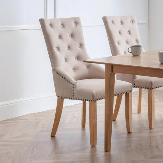 Two beige upholstered chairs with wooden legs around a wooden dining table.