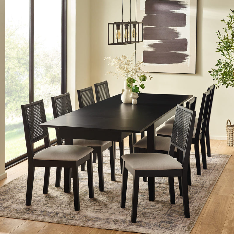Dining room with a black table and chairs on a rug, large windows, and abstract art on the wall.