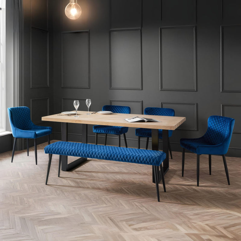 Dining room with blue chairs and bench around a wooden table against a dark paneled wall.