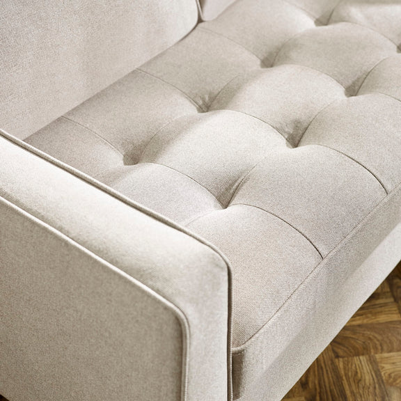 Close-up of a beige tufted sofa with wooden floor in the background
