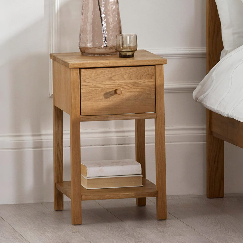 Wooden nightstand with a drawer and small shelf against a neutral wall.