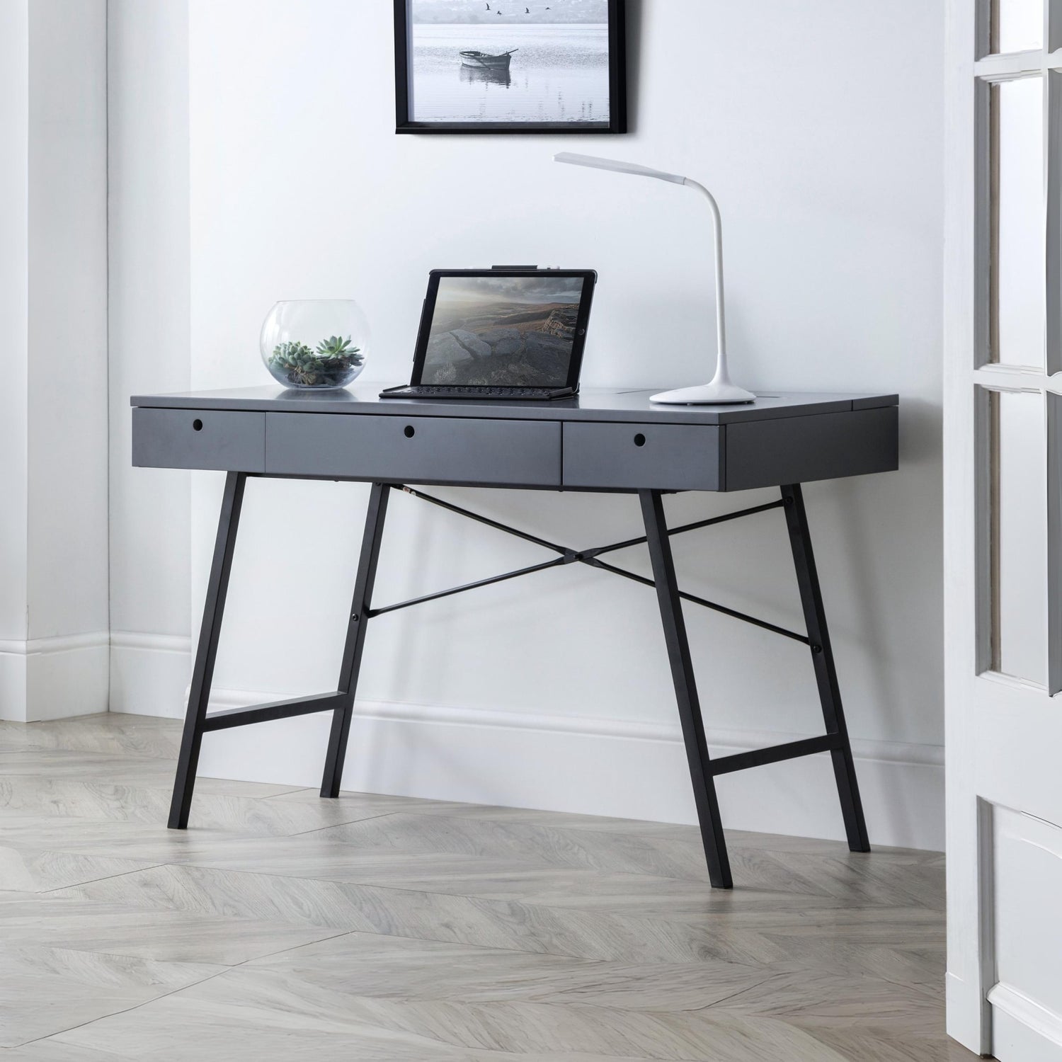 Modern black desk with a laptop and lamp in a minimalistic room.