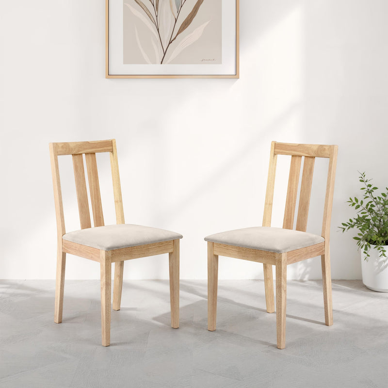 Two wooden chairs with beige cushions in a room with a plant and framed picture on the wall.