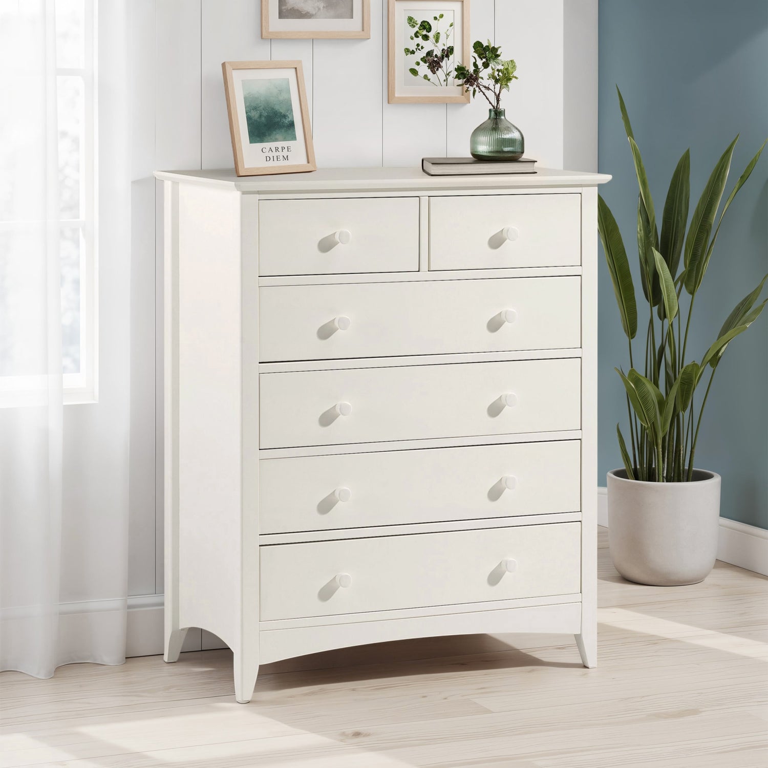 White dresser with decorative items in a room with a plant and framed pictures.