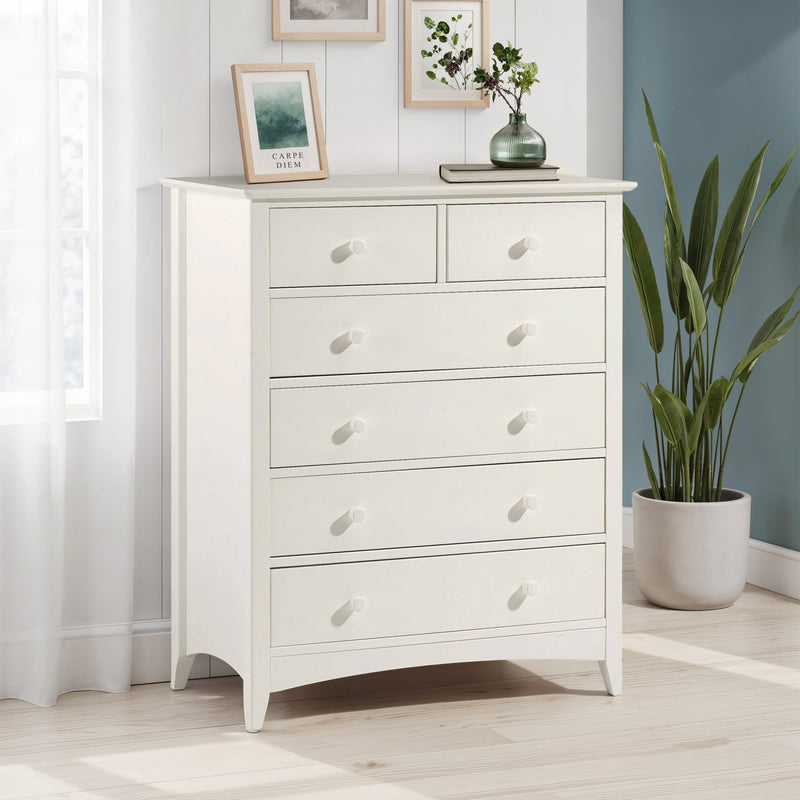 White dresser with decorative items in a room with a plant and framed pictures.