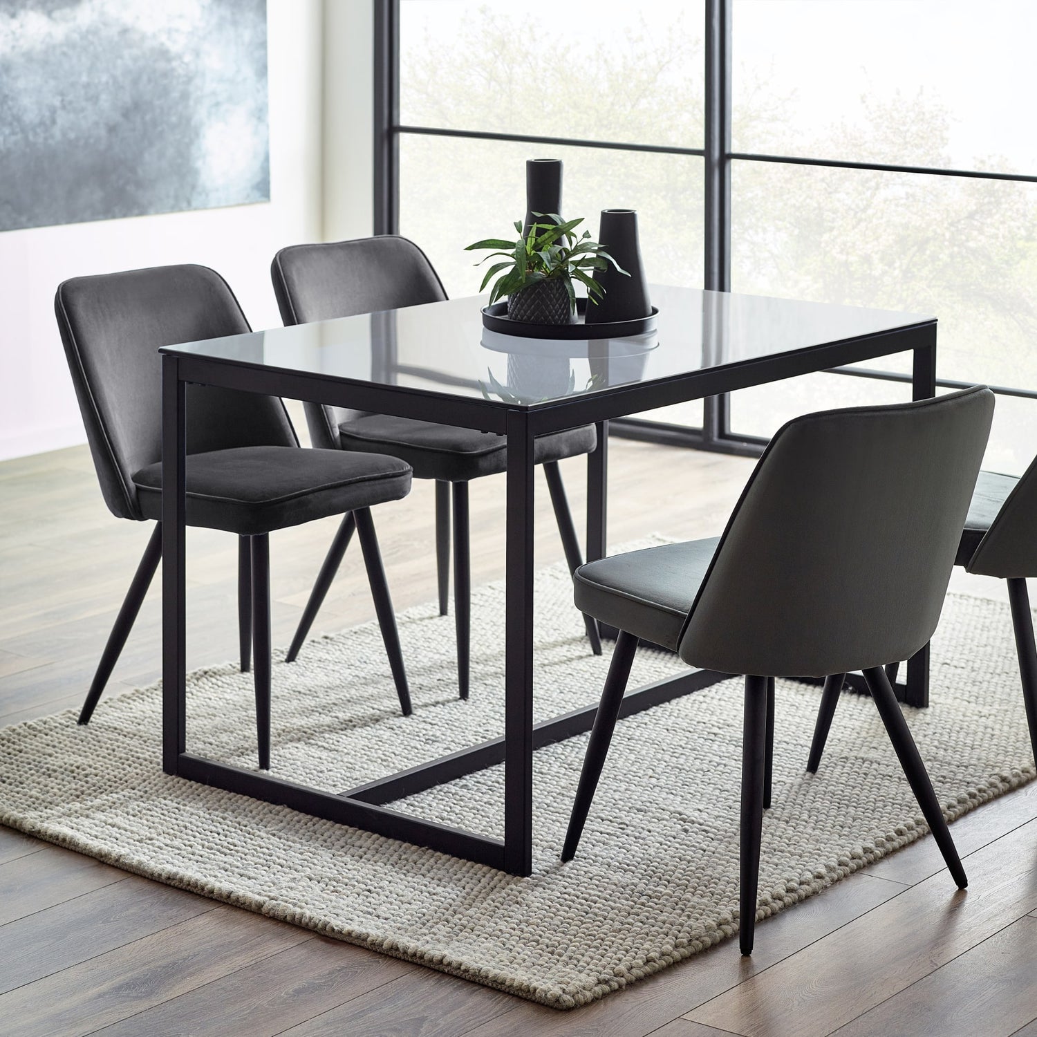 Dining table with four chairs in a modern room with large windows.