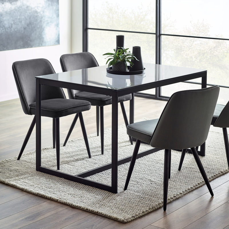 Dining table with four chairs in a modern room with large windows.