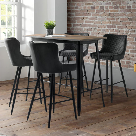 High table with black bar stools in a room with a brick wall and large window.