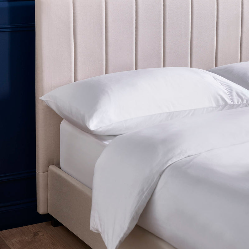 Close-up of a bed with white bedding and pillows against a beige headboard.