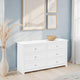 White dresser with six drawers in a room with light blue walls, framed artwork, and a vase with dried plants.