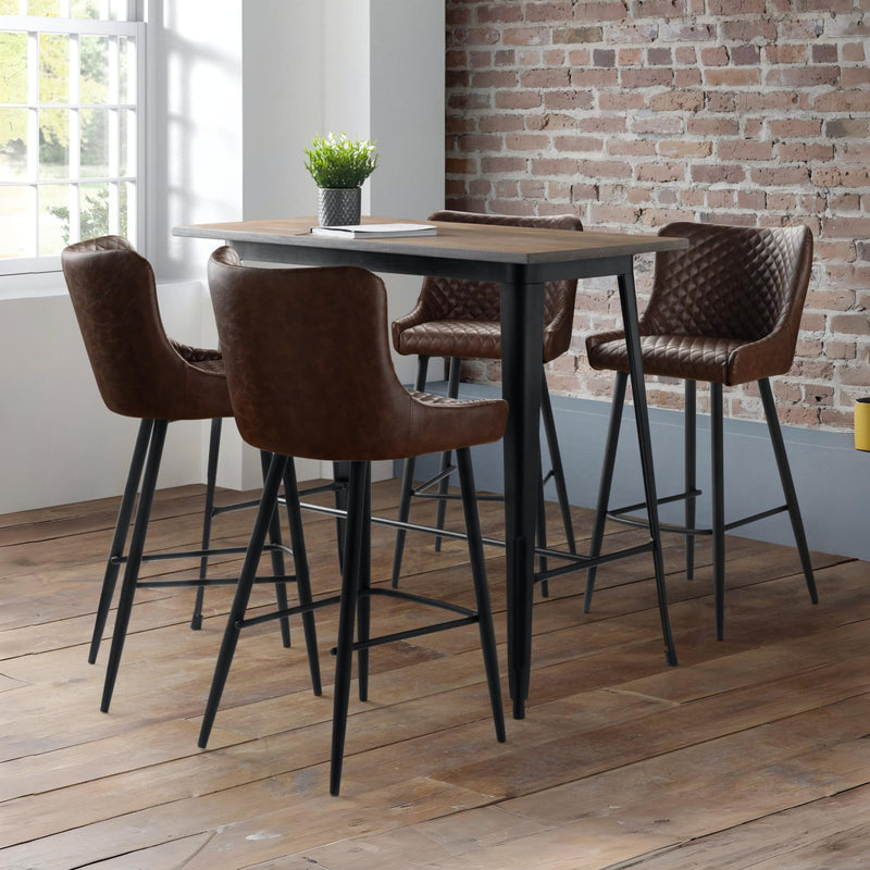 Bar height table with brown leather stools in a room with brick wall and window.