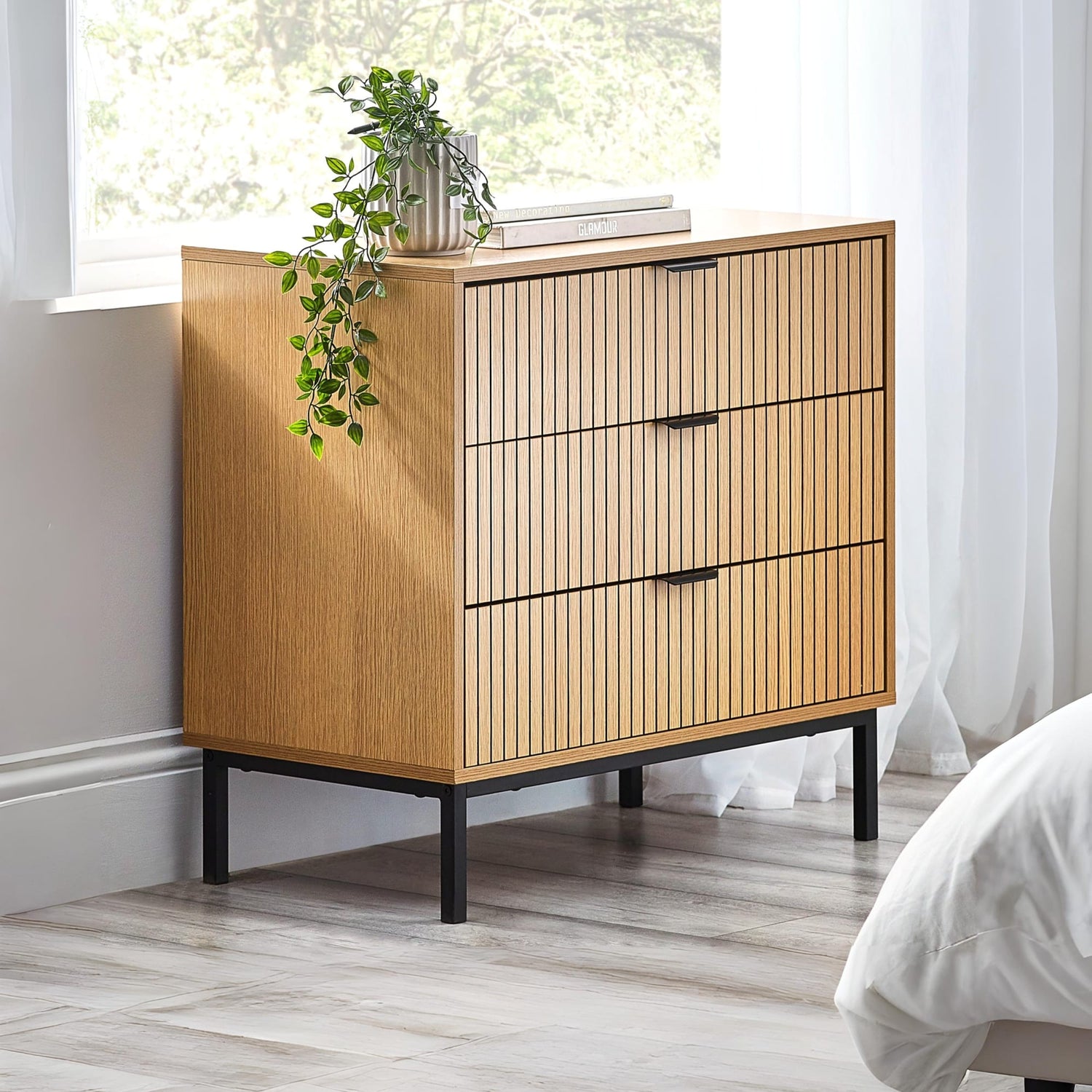 Wooden dresser with black legs in a room with a window and plant