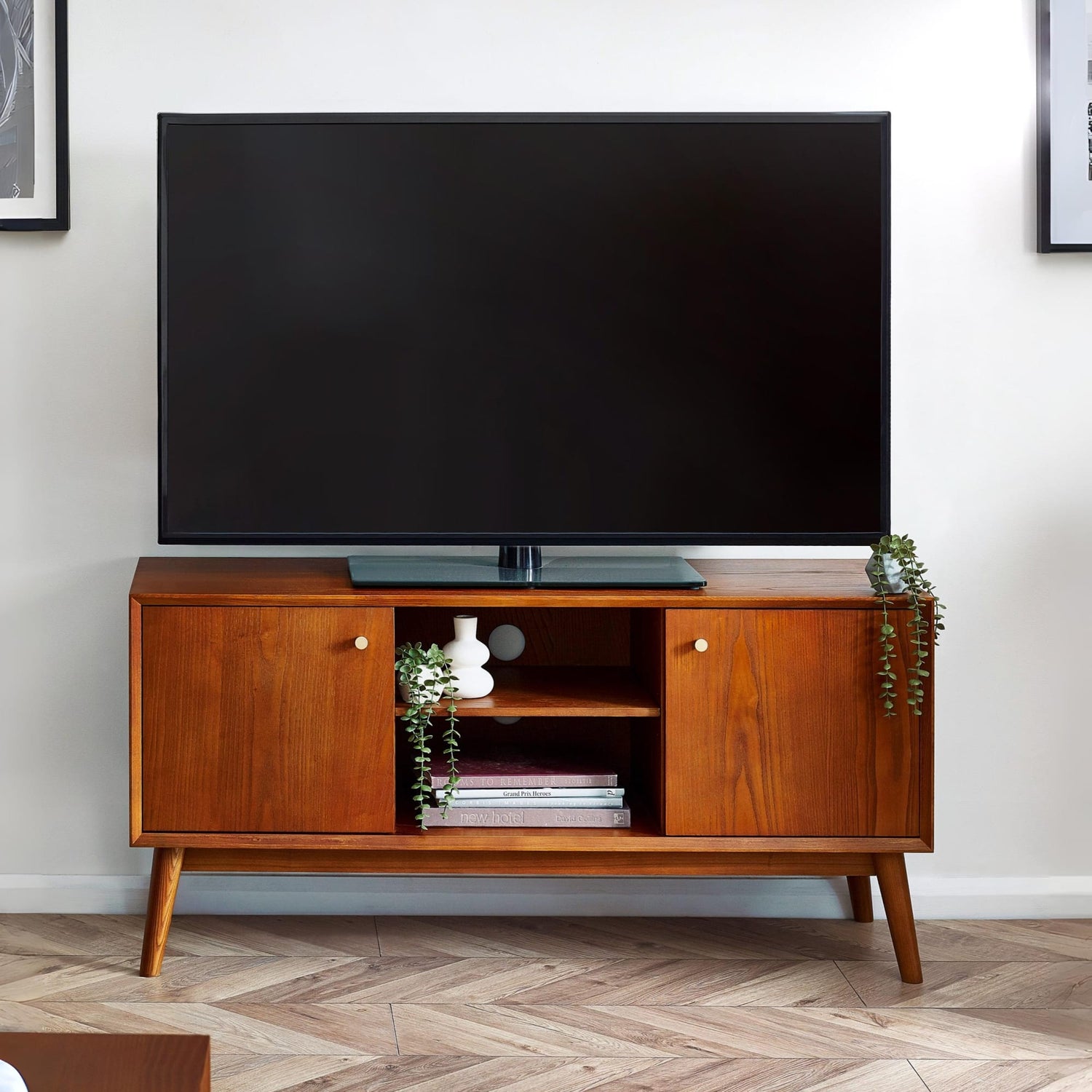 Wooden TV stand with a large flat-screen TV on top in a room with a white wall and wooden floor.