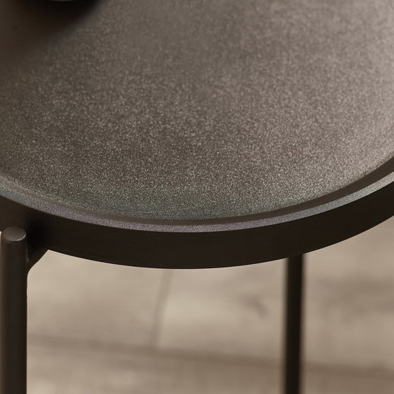 Close-up of a round table with textured surface and black metal legs.