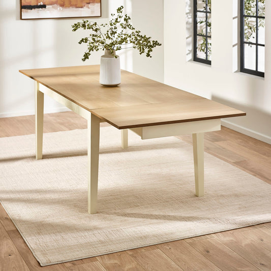 Wooden dining table with a vase of greenery on a light wooden floor.