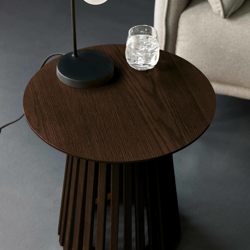 Round wooden side table with a lamp and glass on a gray floor.