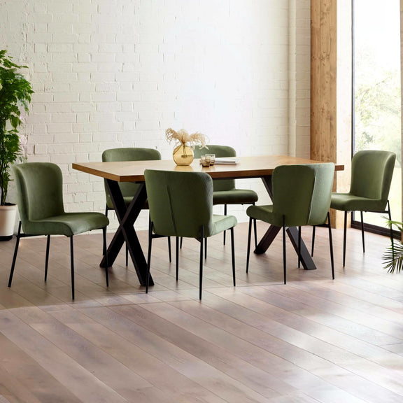 Dining table with green chairs in a modern room with white brick wall and large window.