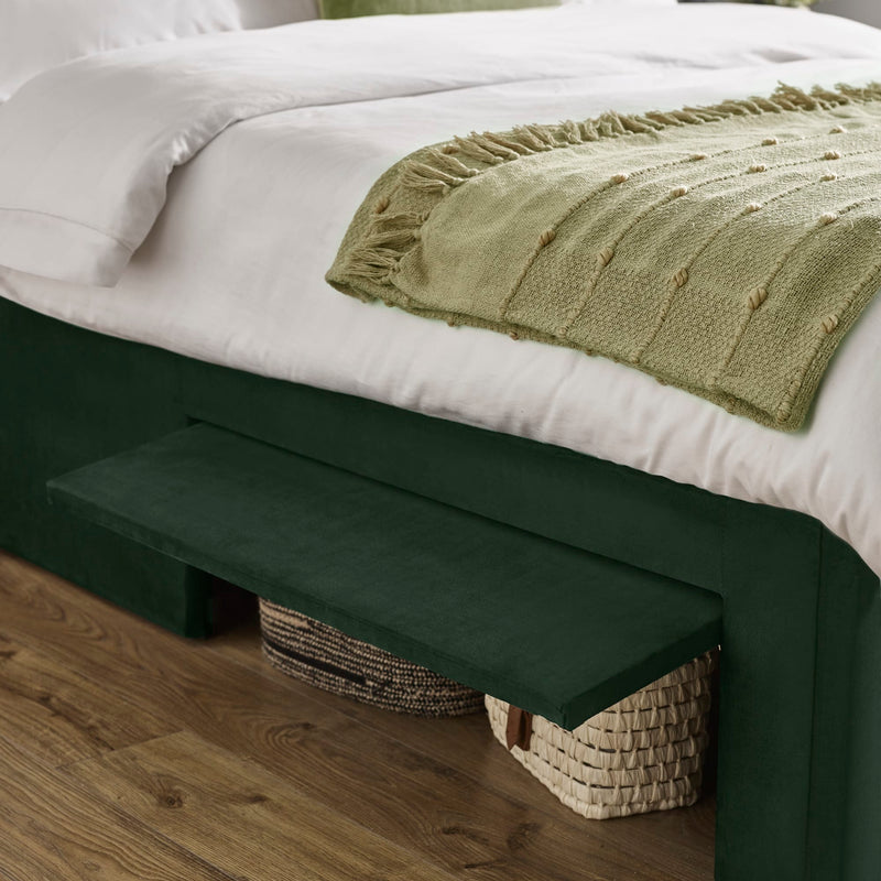 Green footstool next to a bed with white bedding and a green blanket.