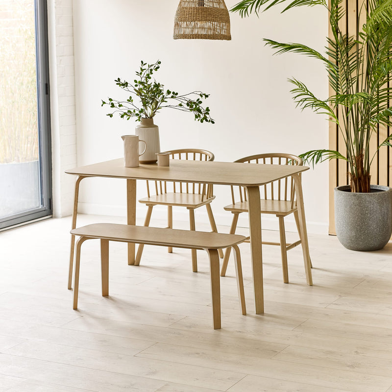 Dining area with wooden table, chairs, and bench in a bright room with plants.