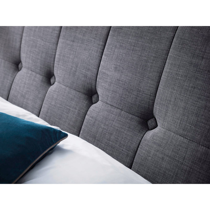 Gray tufted headboard on a bed with a white mattress and blue pillow.