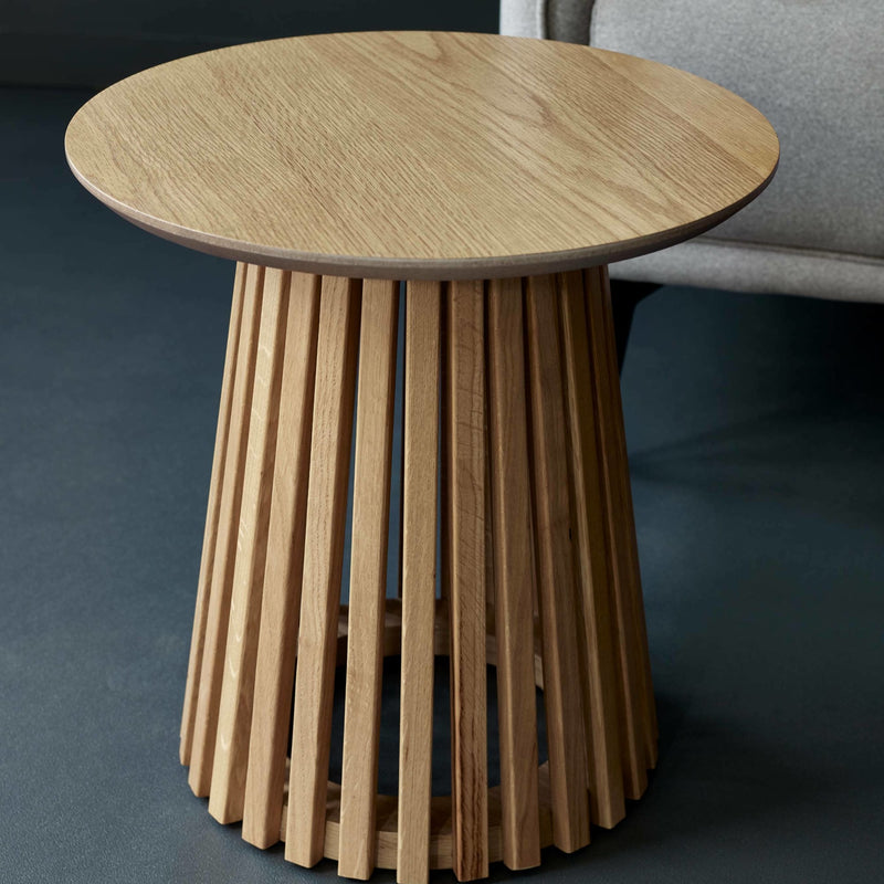 Wooden side table with a unique cylindrical base design against a dark background.