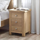 Wooden nightstand with three drawers next to a bed in a bedroom setting.