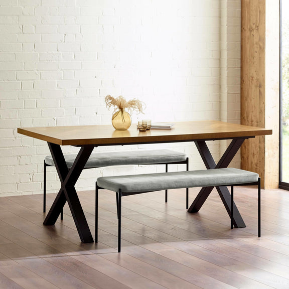 Dining table with two benches in a room with white brick walls and wooden flooring.