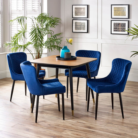 Dining room with a wooden table and blue chairs, featuring a plant and framed pictures on the wall.